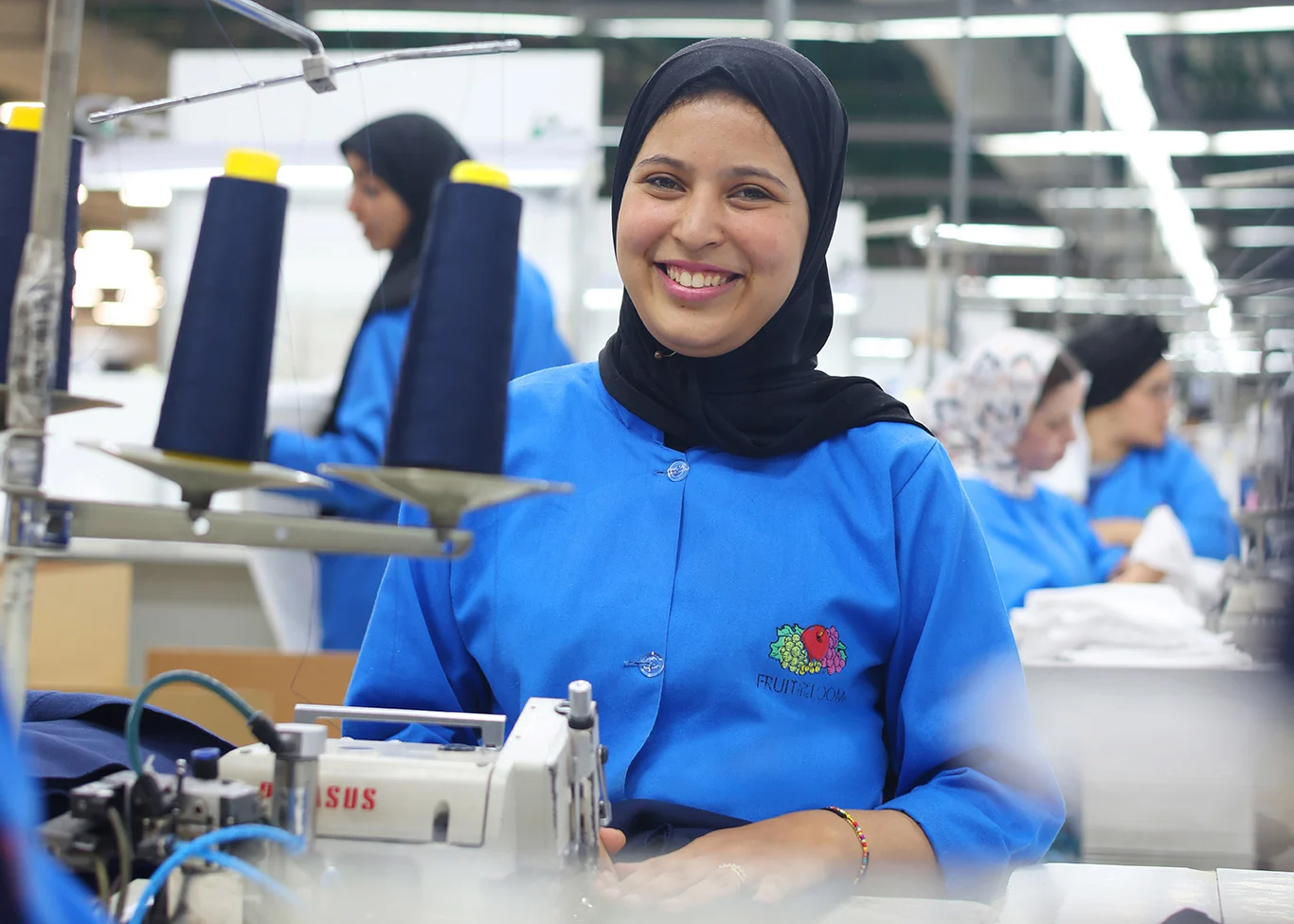 A woman is smiling and working at a sewing machine.