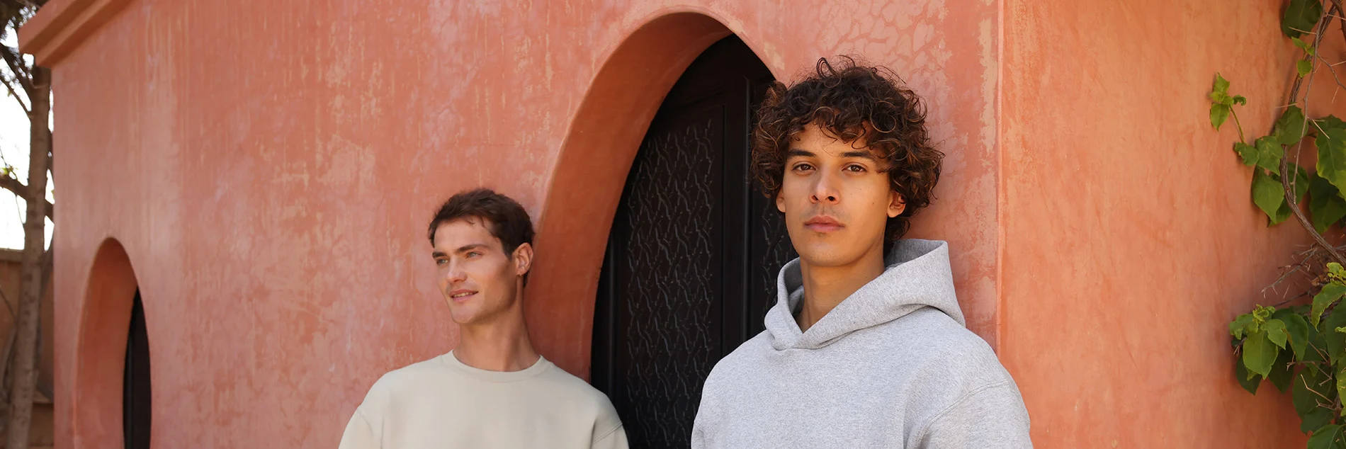 Two male models pose in front of a large curved doorway wearing our sweatshirt sets.