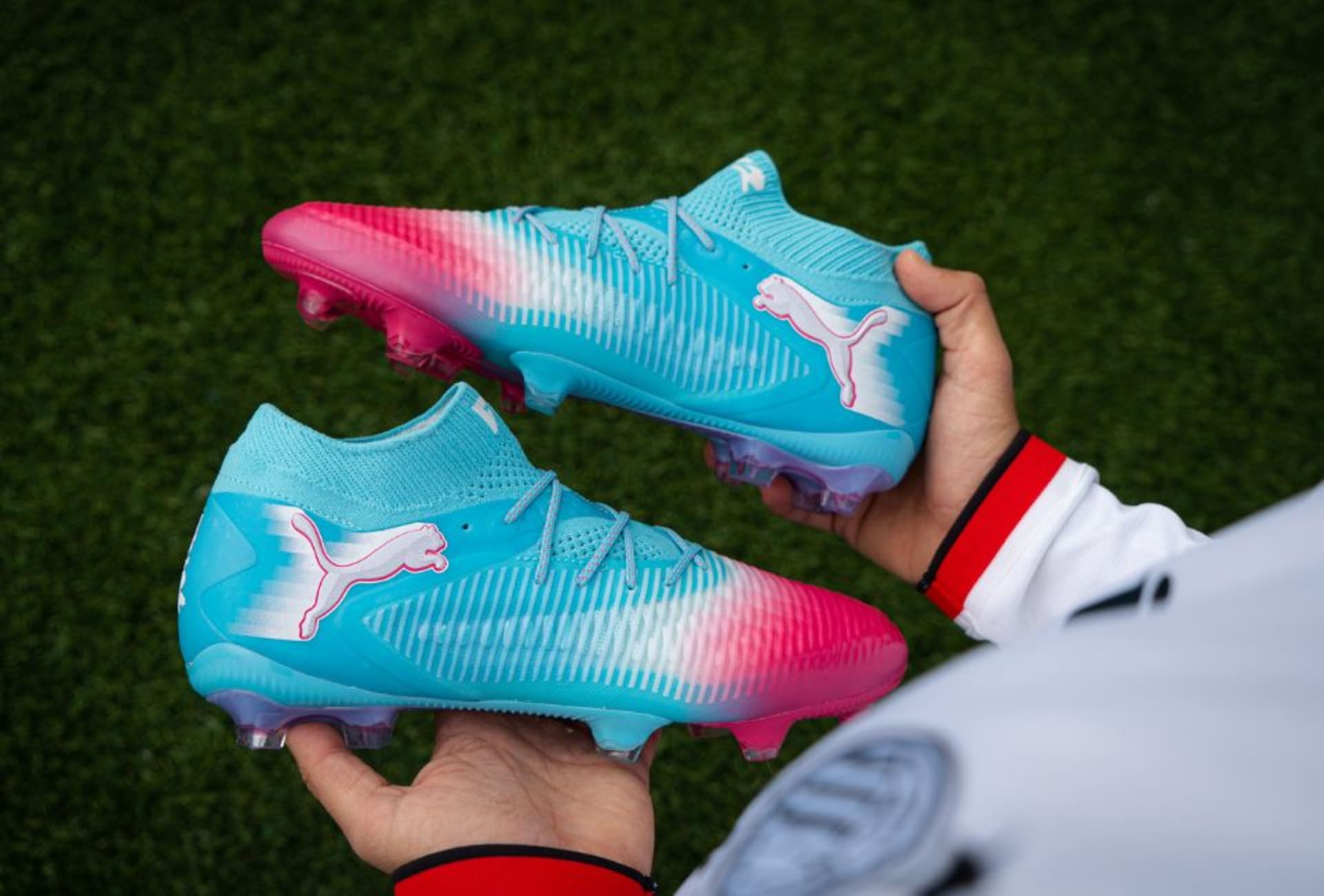 Zwei Paar Puma Re-Charge Fussballschuhe stehen nebeneinander auf dem Rasenplatz.