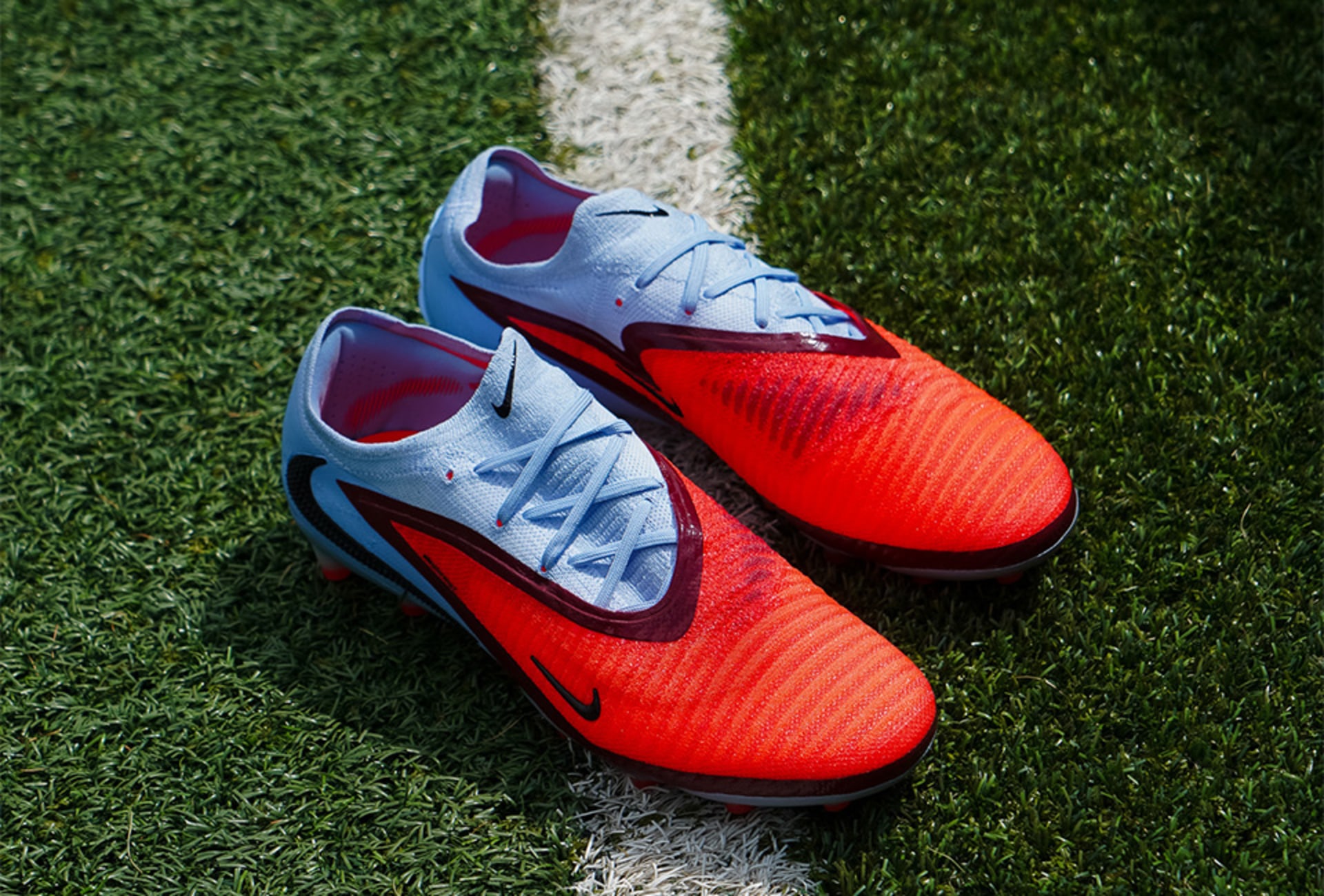 Ein Paar weisse Nike Gear Up Fussballschuhe mit orangem Akzent auf Rasen.