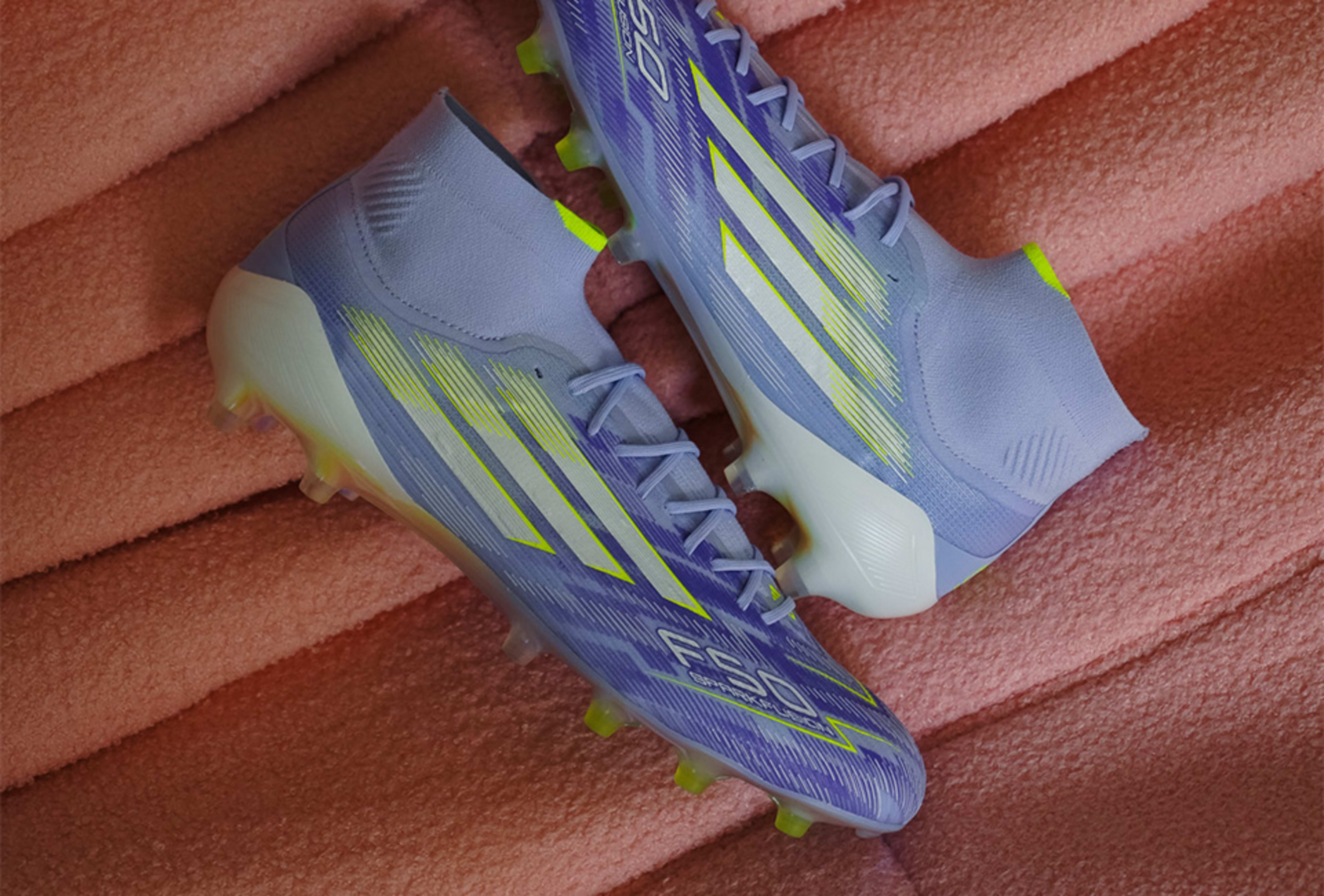 Ein Paar Adidas Sparkfusion Fussballschuhe auf rosa Hintergrund.