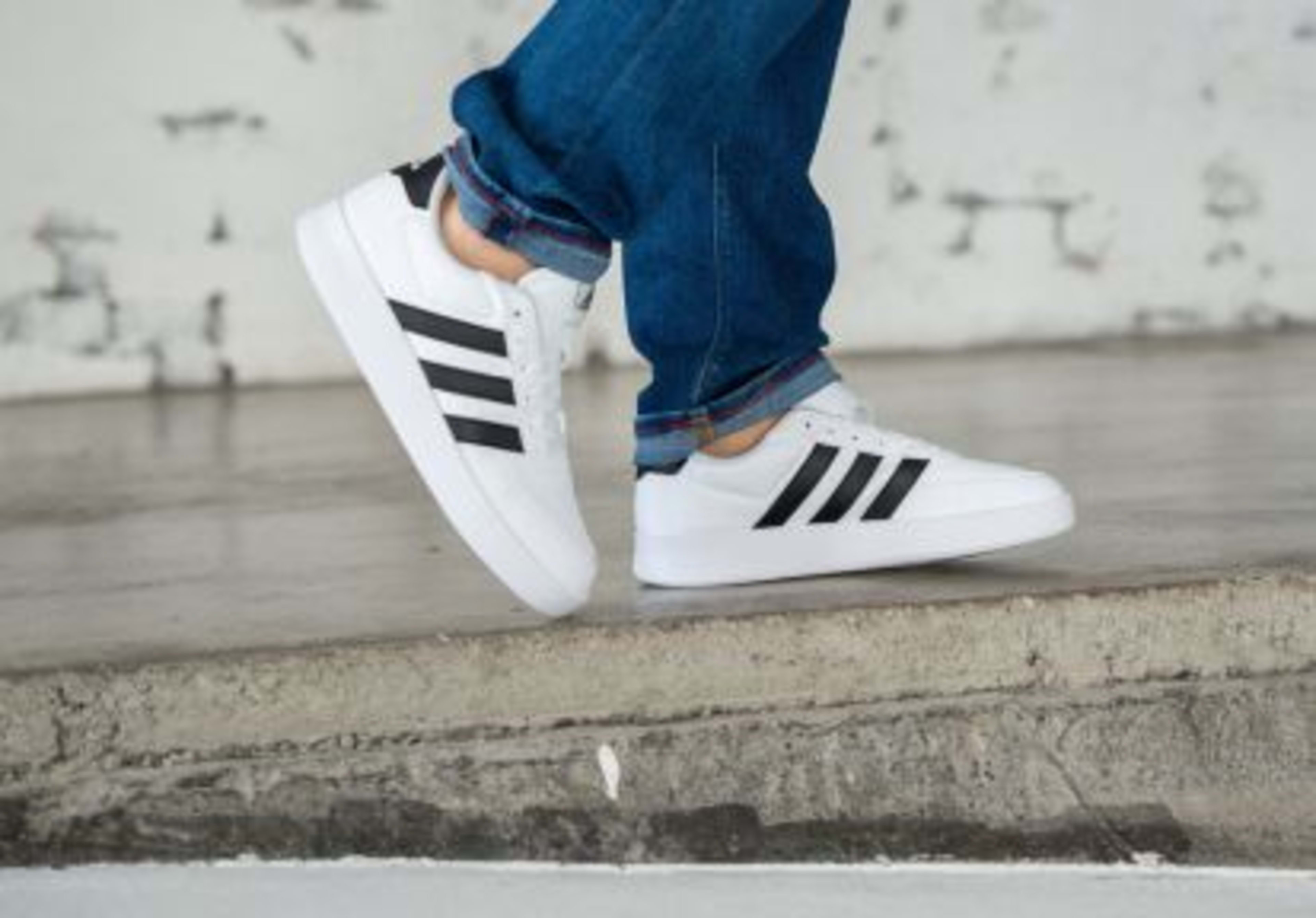 Mann traegt Adidas Originals in weiß mit schwarzen Streifen am Fuss.