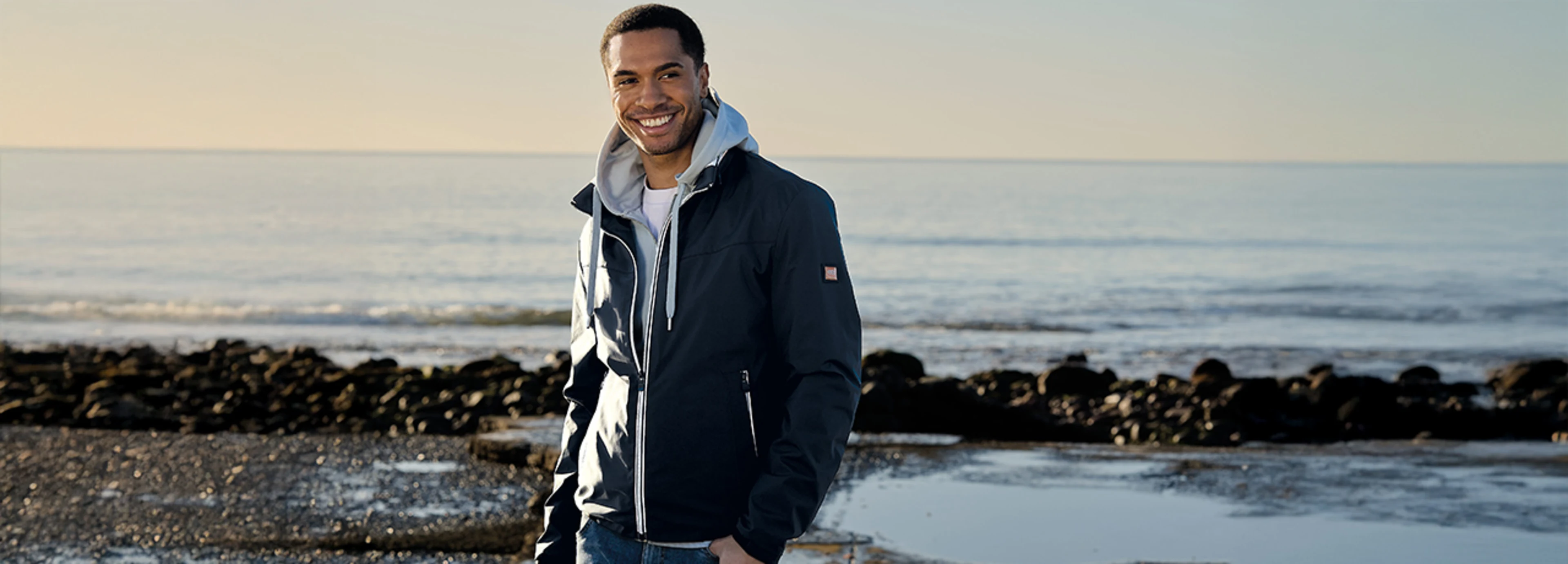 Stylische Jacke für Herren in hellgrau, kombiniert mit einem weißen Basic T-Shirt und einer hellblauen Sweatjacke