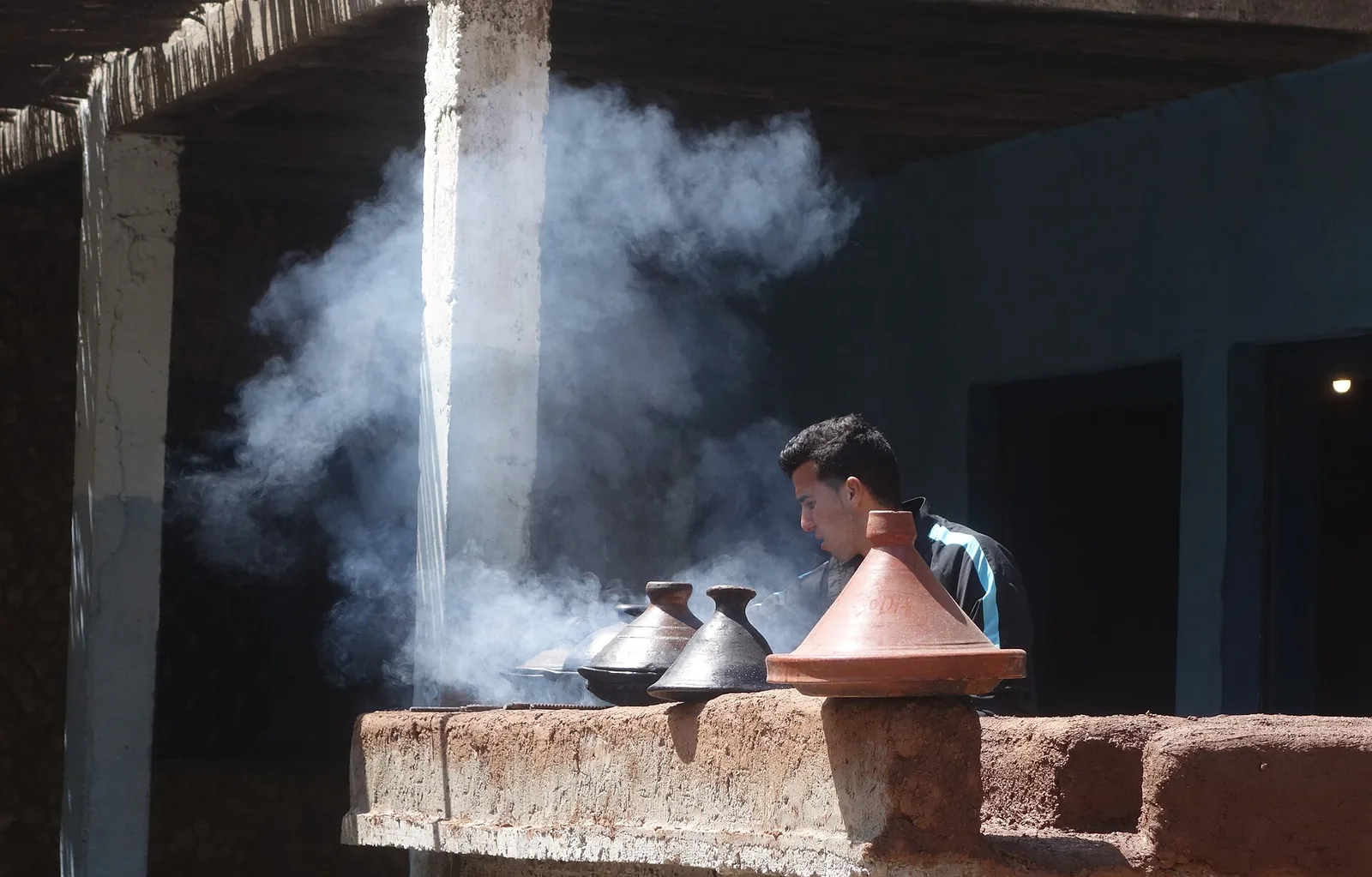 Cook preparing clay tajines in a smoky Moroccan kitchen