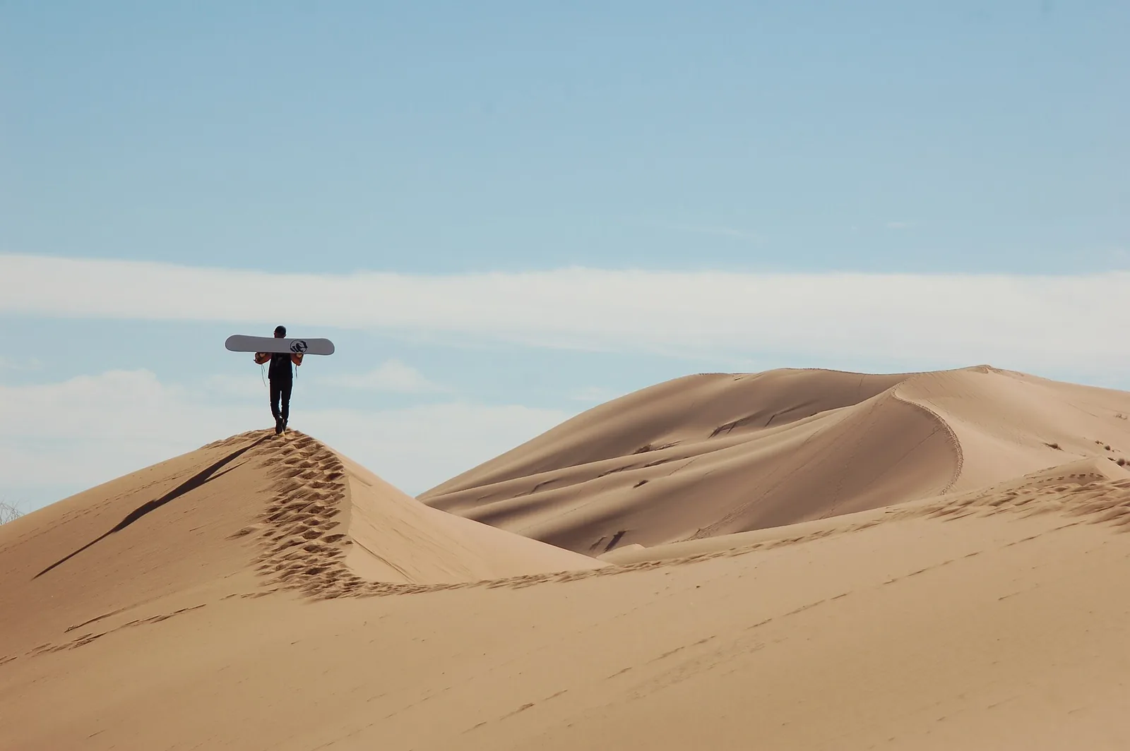 Person carrying a board on top of a sand dune in Erg Chebbi