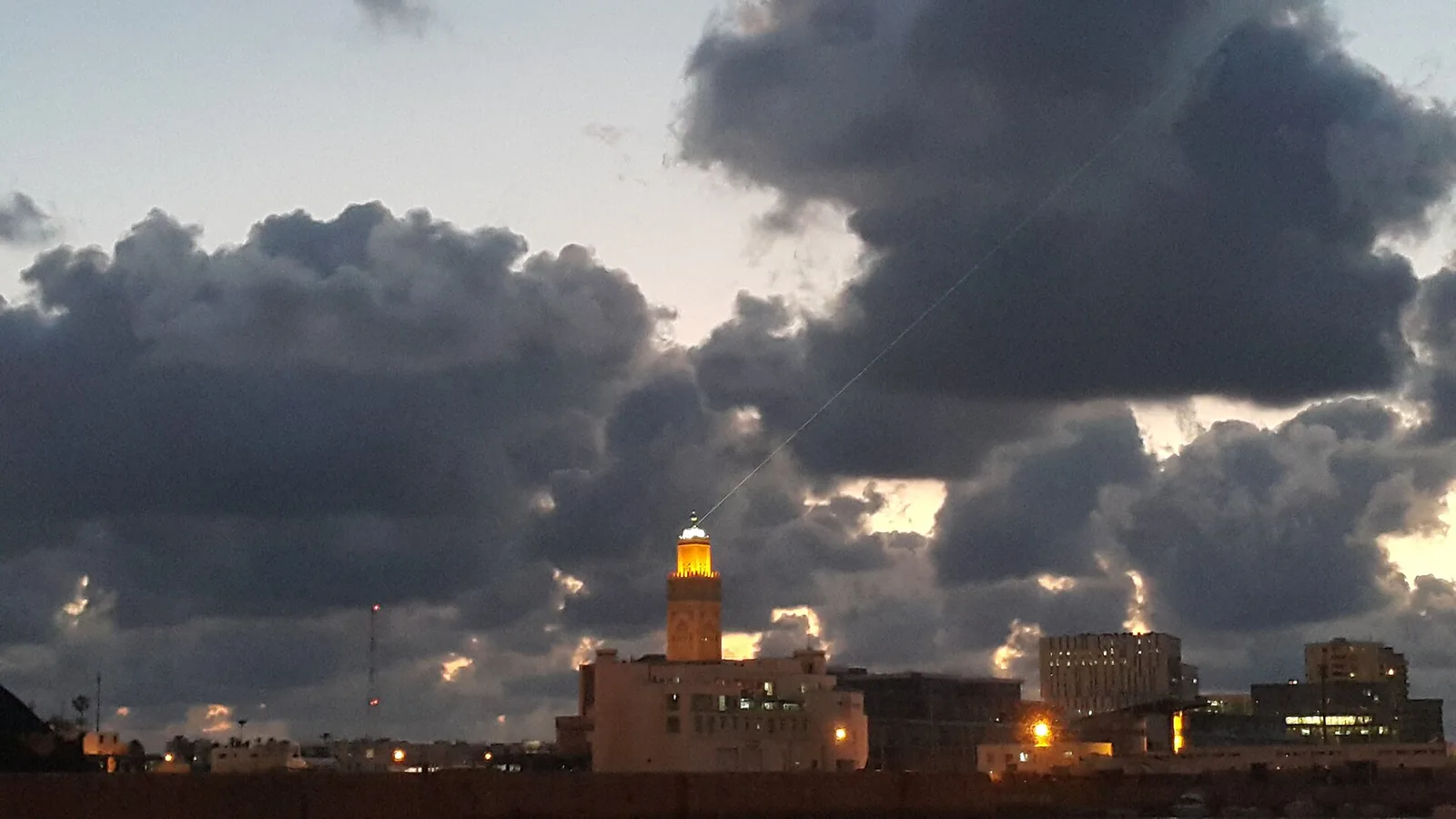 Hassan II Mosque minaret lit at dusk under stormy clouds