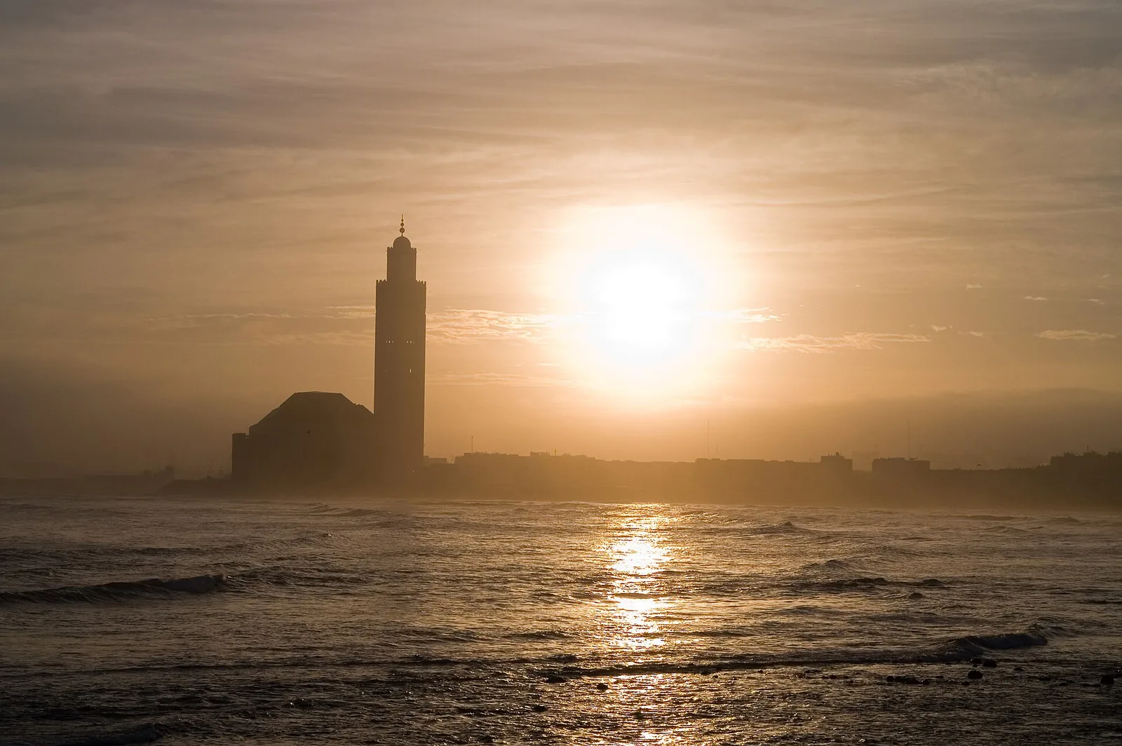 Hassan II Mosque silhouetted against the sunset over the ocean