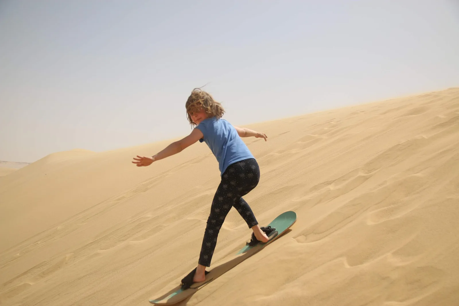 Sandboarder riding down a sand dune