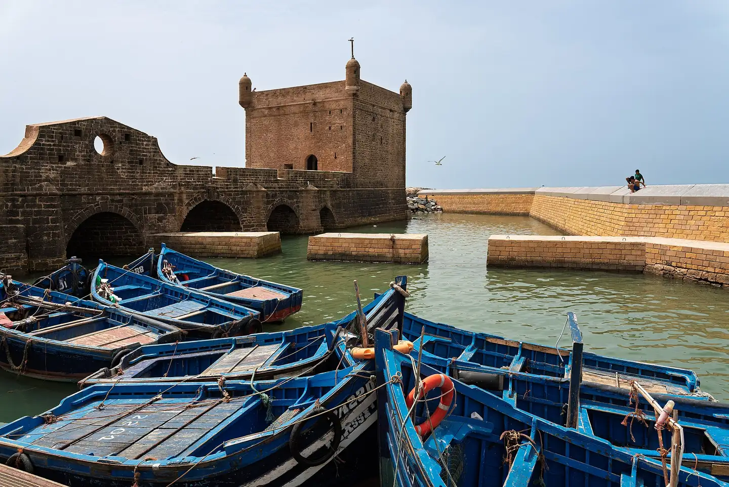 Blue fishing boats moored below the sea fortress in Essaouira harbour