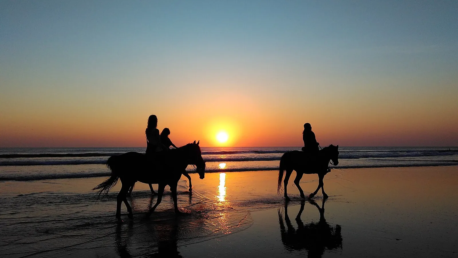 Two riders on horseback on a beach at sunset