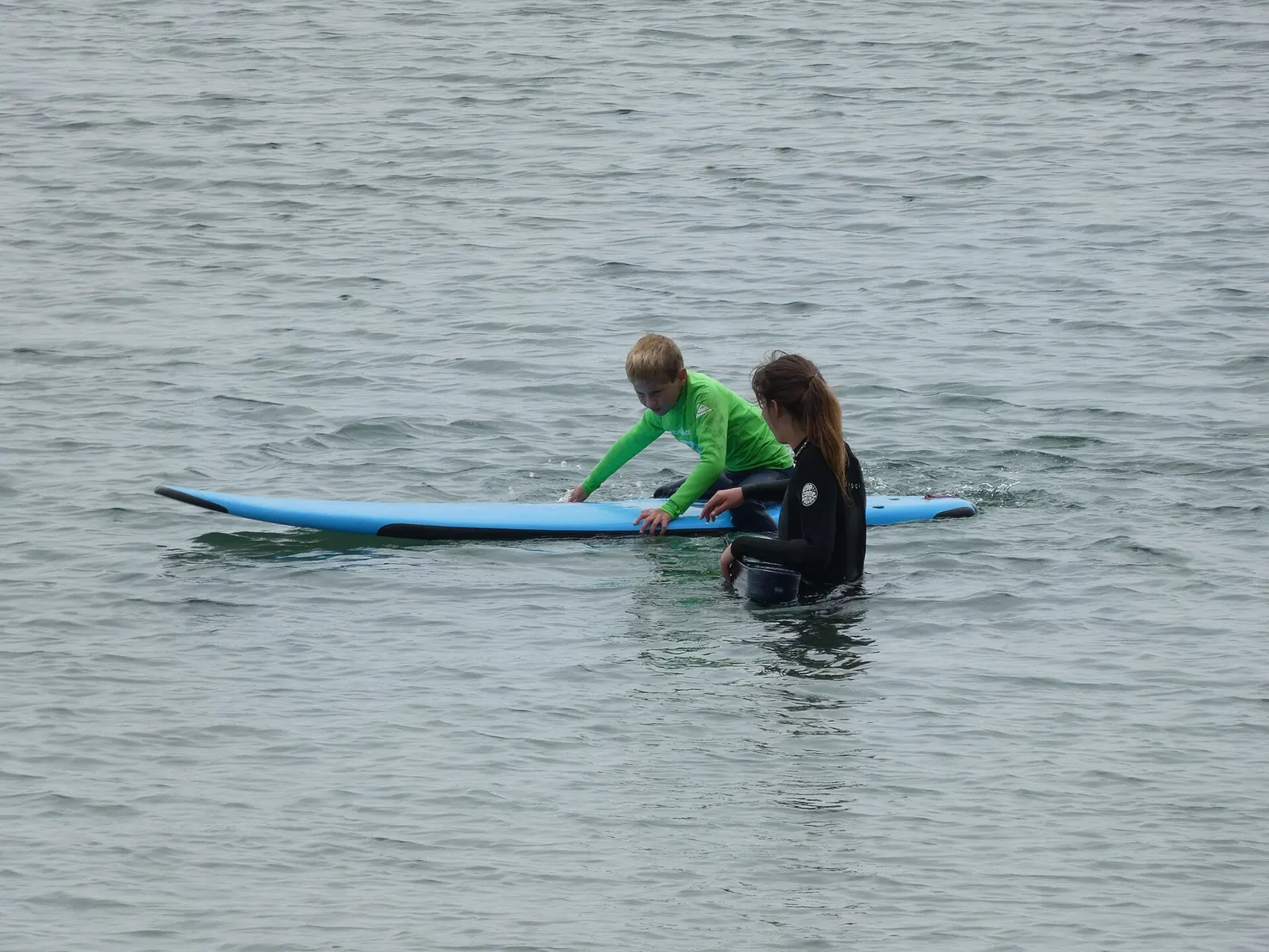 Surf instructor helping a beginner on a board in shallow water