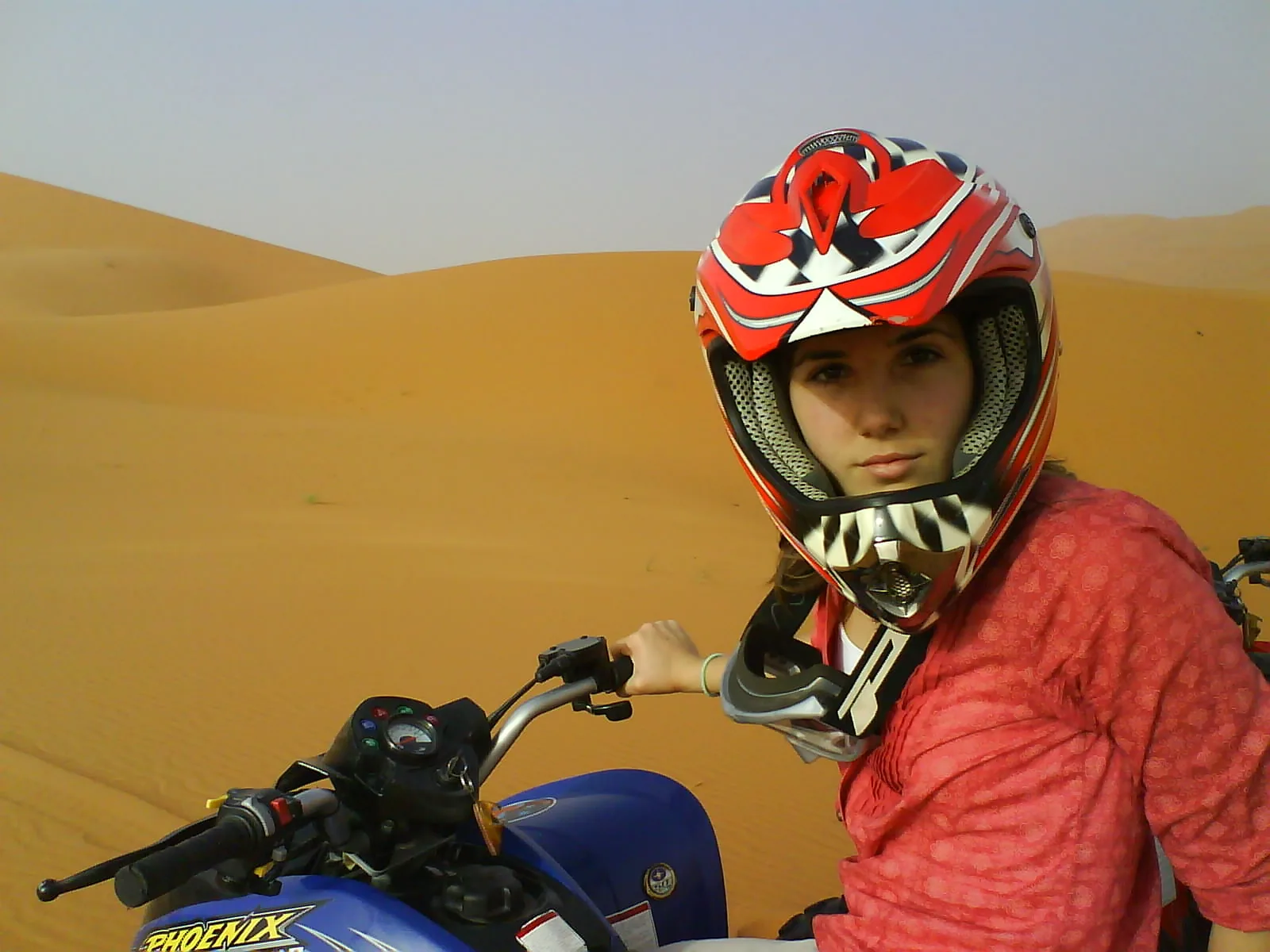A rider in a red helmet on a quad bike in the dunes