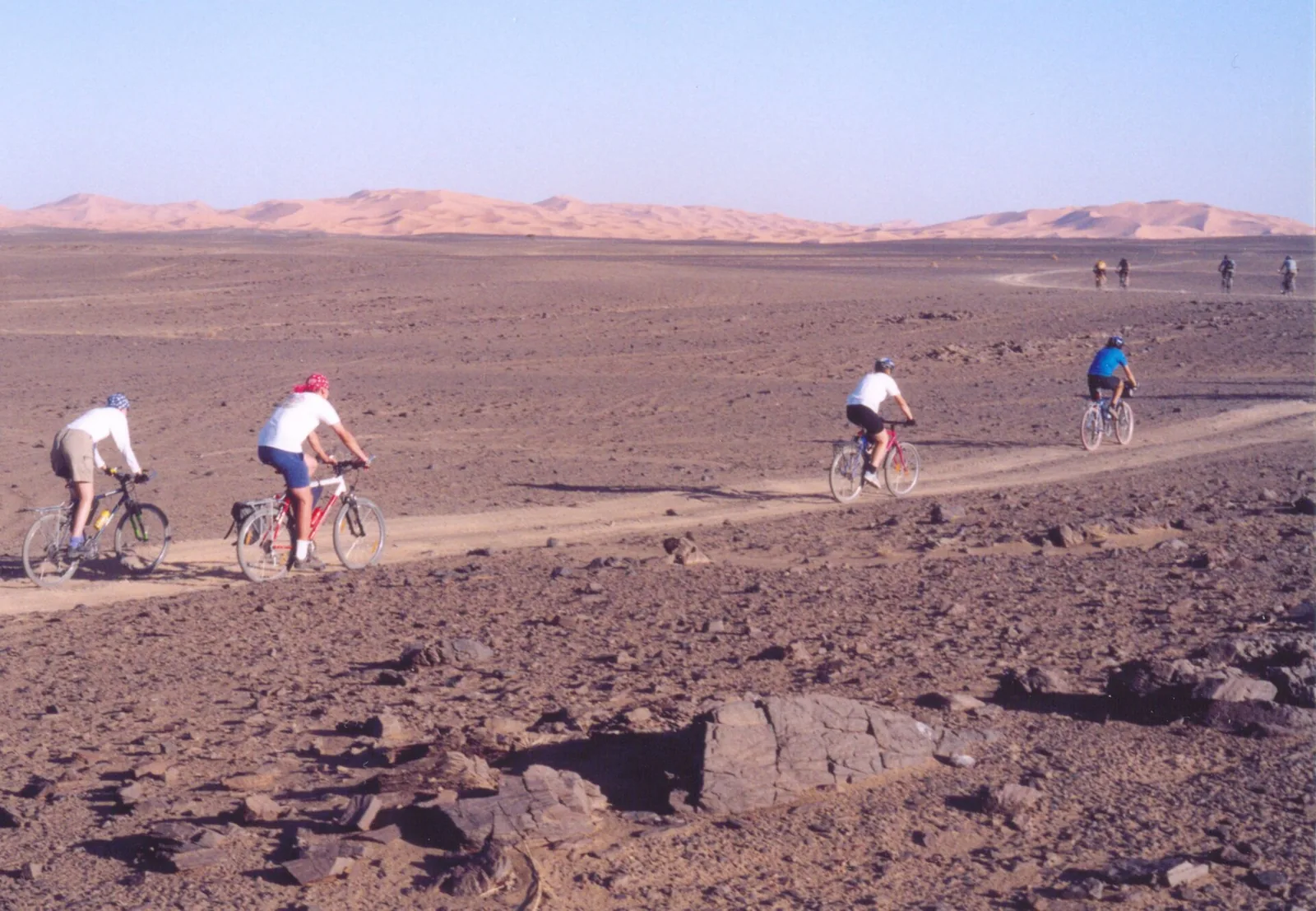 Cyclists crossing the stony plain with the Erg Chebbi dunes behind