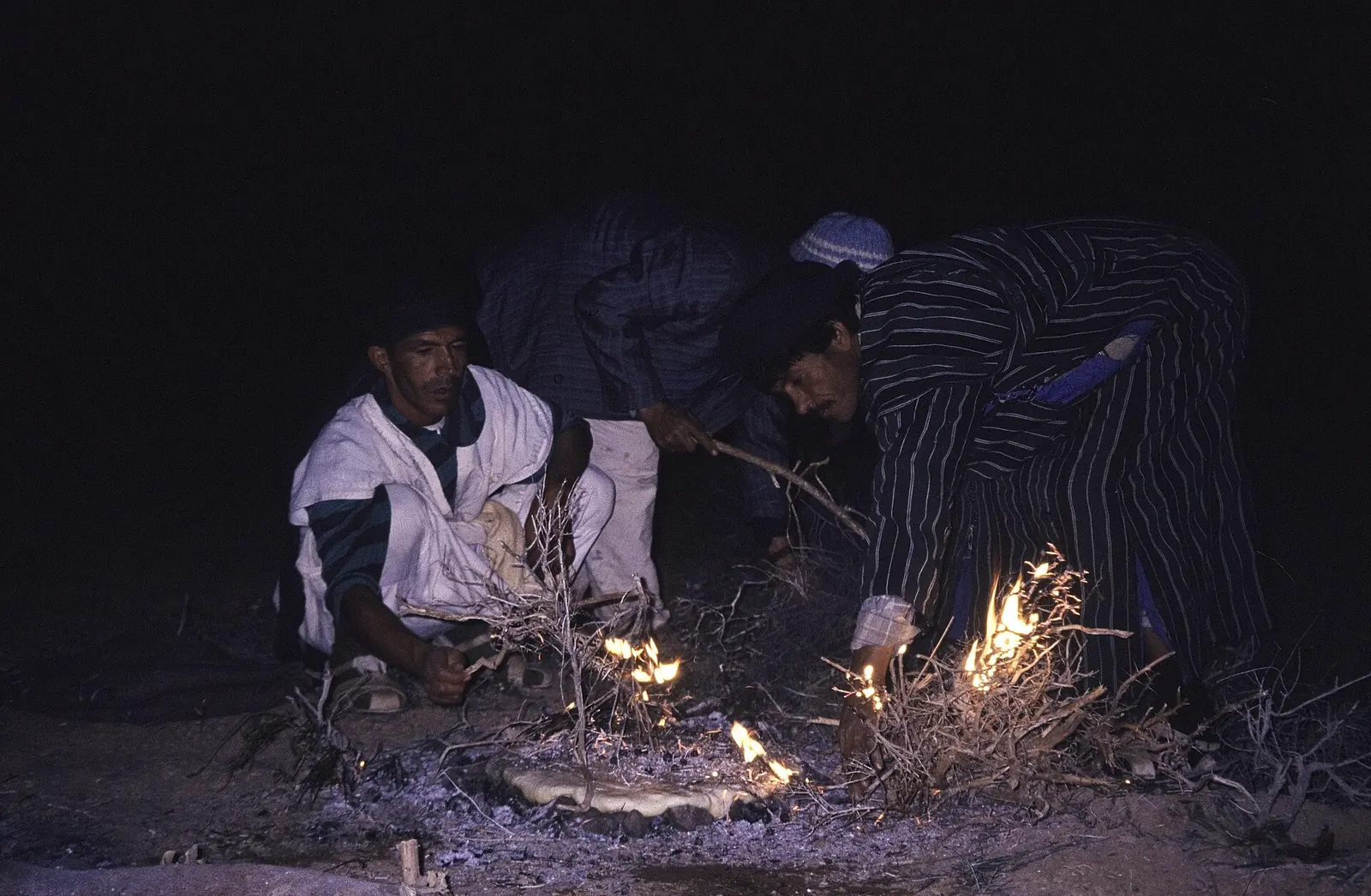 Men baking a round flatbread over embers in Morocco