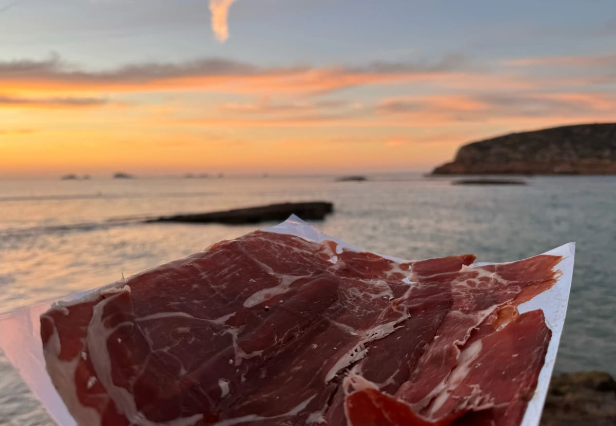 Plato de jamón ibérico loncheado en una terraza frente al mar al atardecer