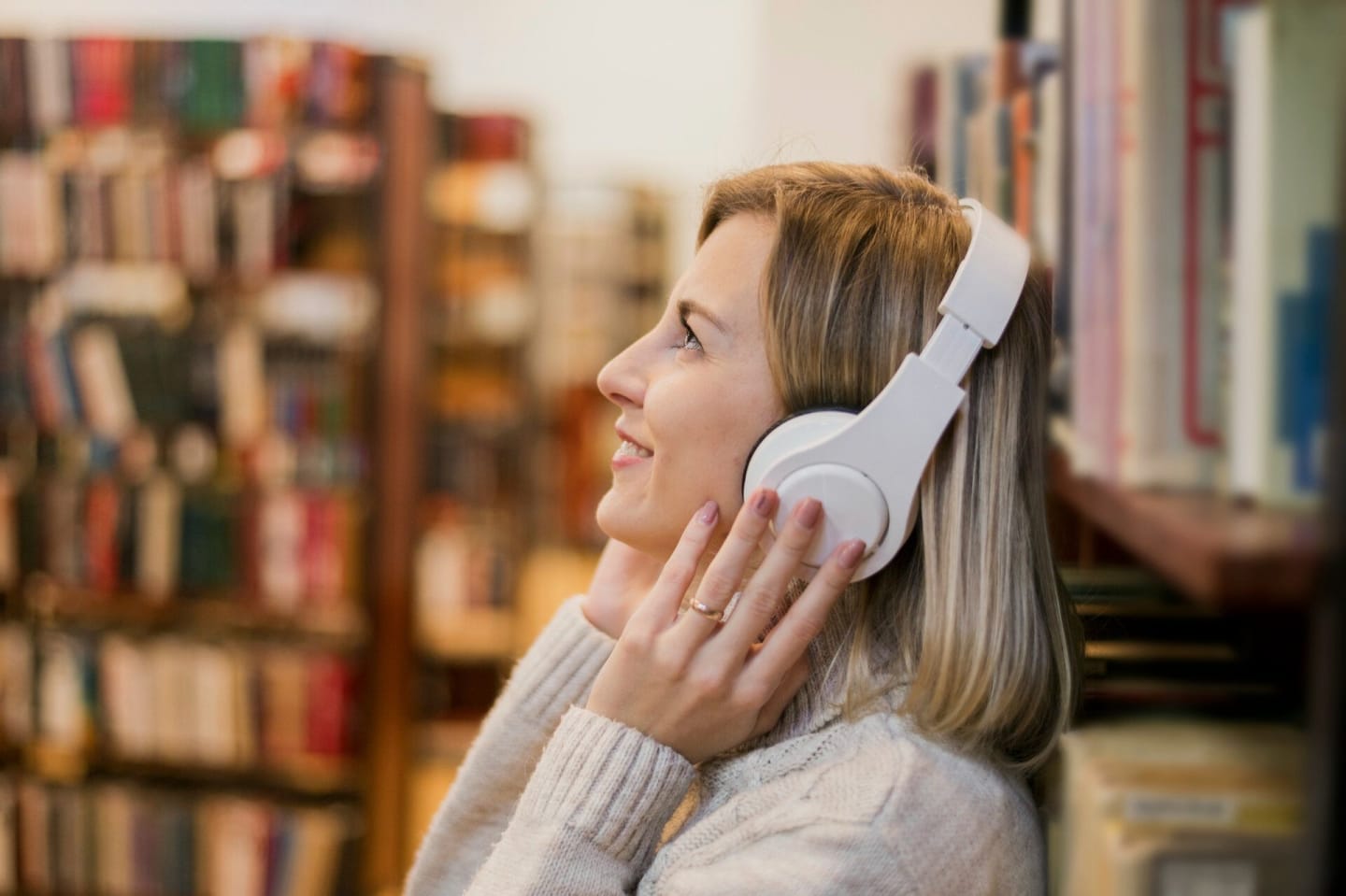 Vrouw met hoofdtelefoon op staat naast een boekenkast