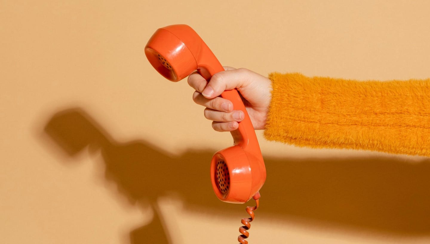 Oranje hoorn van ouderwetse bakelieten telefoon in hand van vrouw met gele trui.