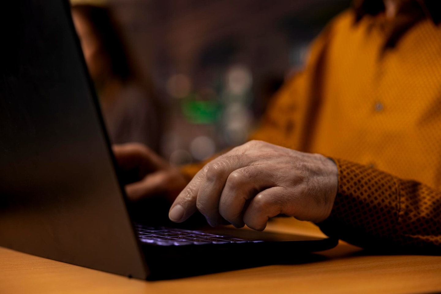 Man in oranje overhemd achter laptop