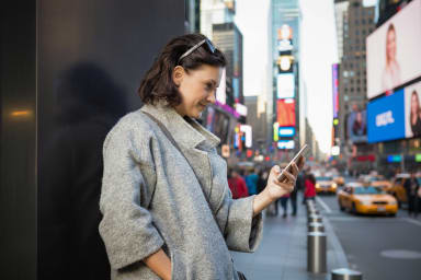 Kobieta korzysta z telefonu stojąc na Time Square w Nowym Jorku, w tle rozmyte budynki i żółte taksówki