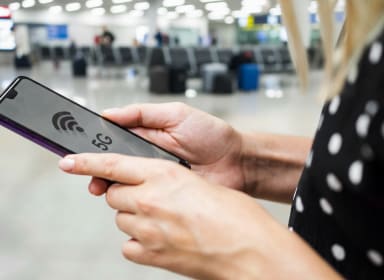 Telefon w dłoniach z wyświetlonym napisem 5G i zasięgiem, w tle rozmyte wnętrze lotniska