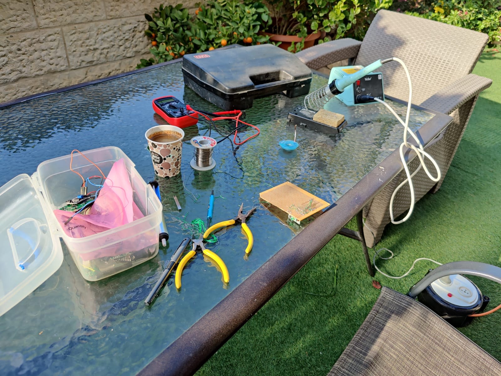 Development workspace with electronic circuits, soldering gear, and coffee