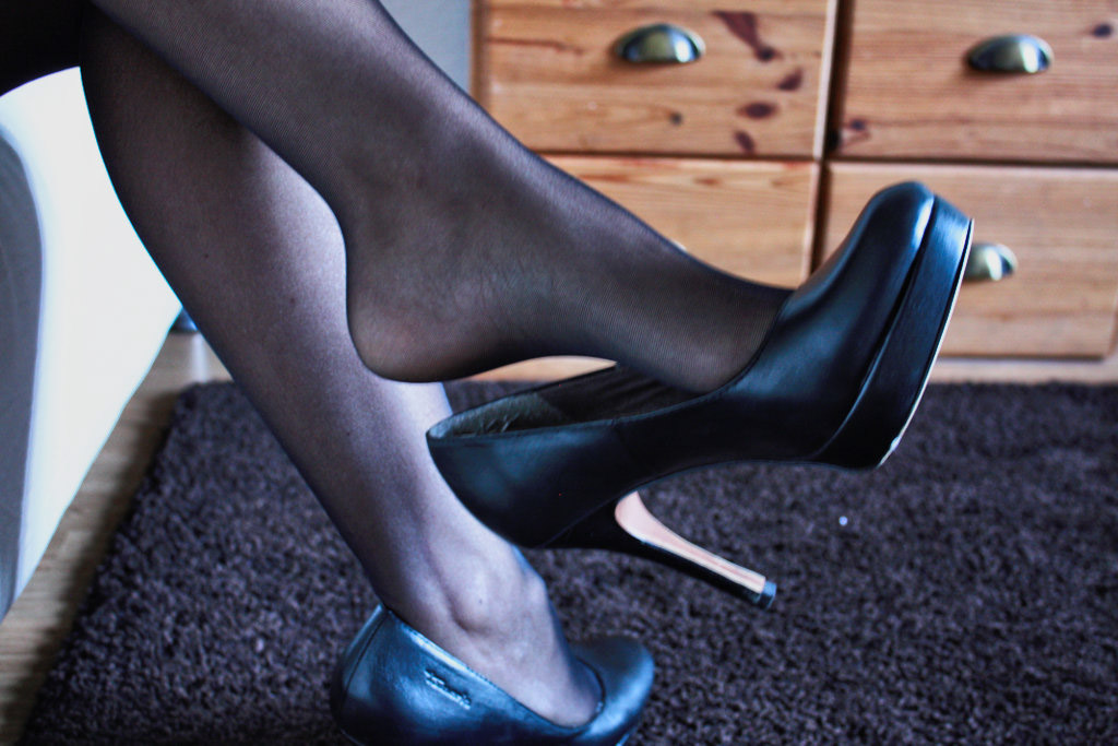 a woman's nyloned clad legs crossed and her shoe dangling from her foot