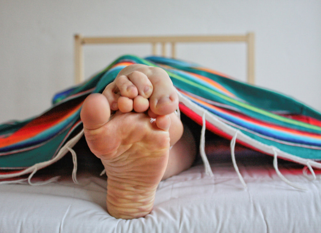 a woman's soles as she lays on a bed covered by a rainbow blanket