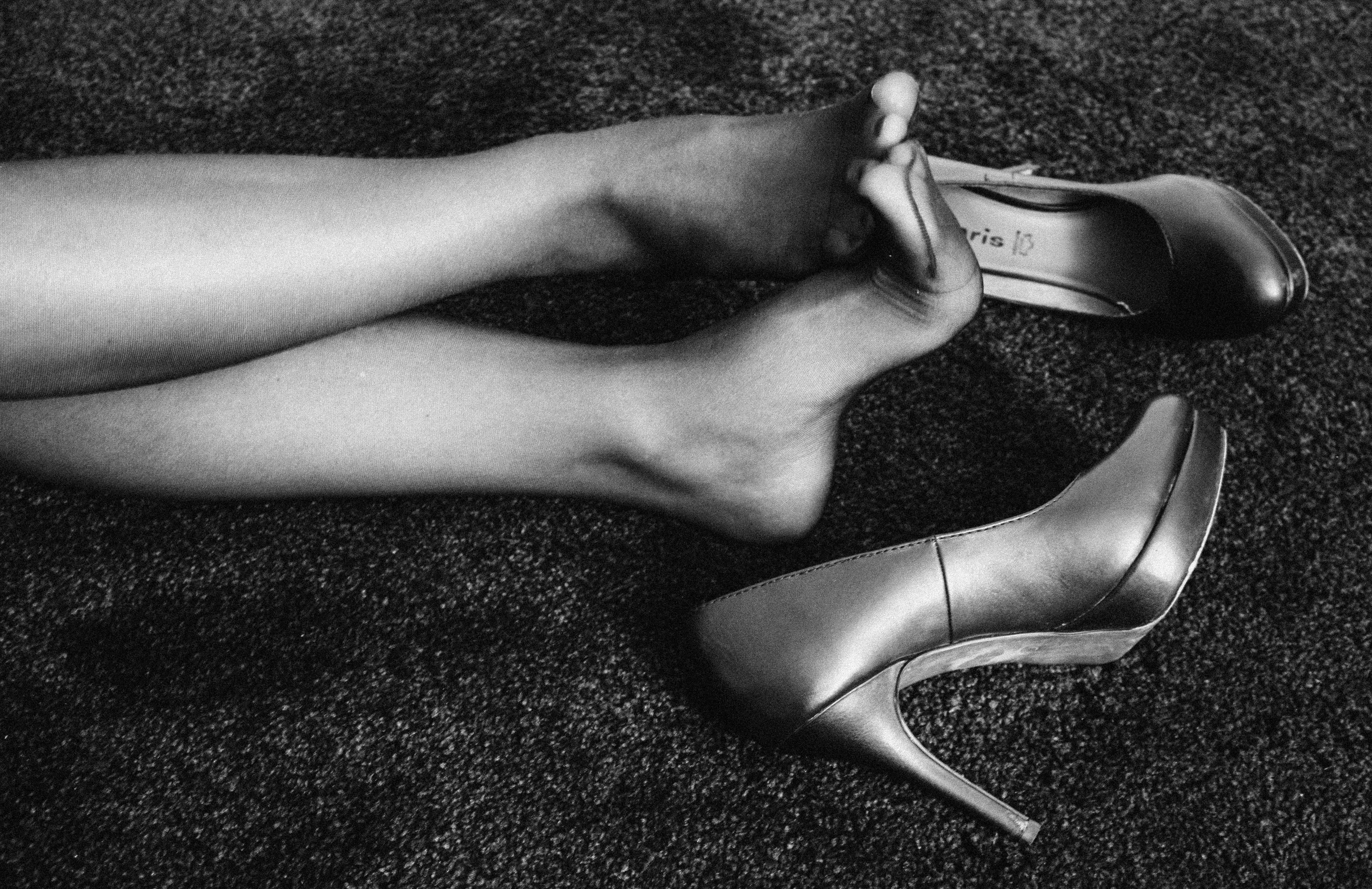 a womans wearing black nylons flexing her arches while her shoes lay next to her feet