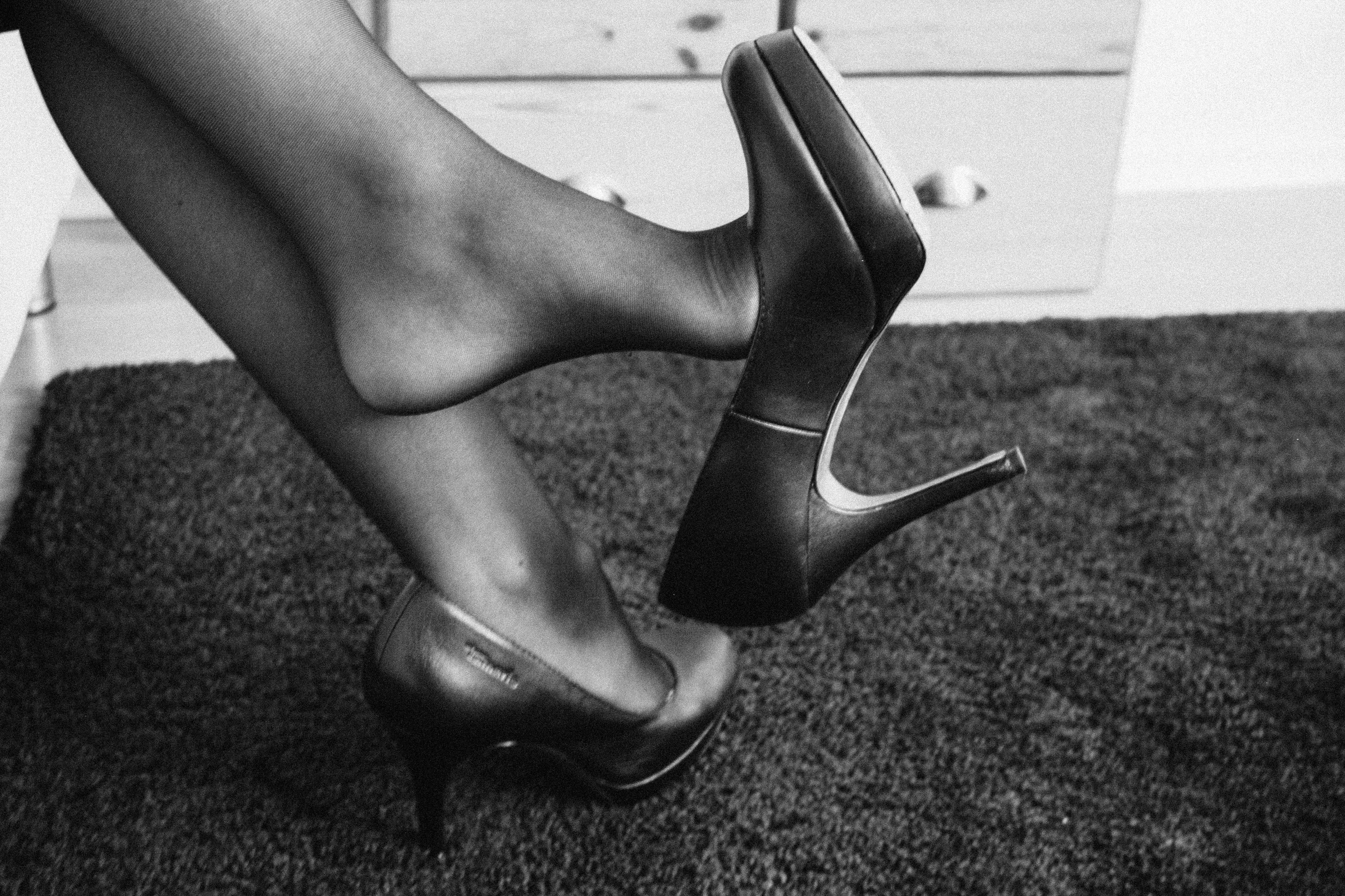 a woman wearing black nylons dangling her shoe from her foot