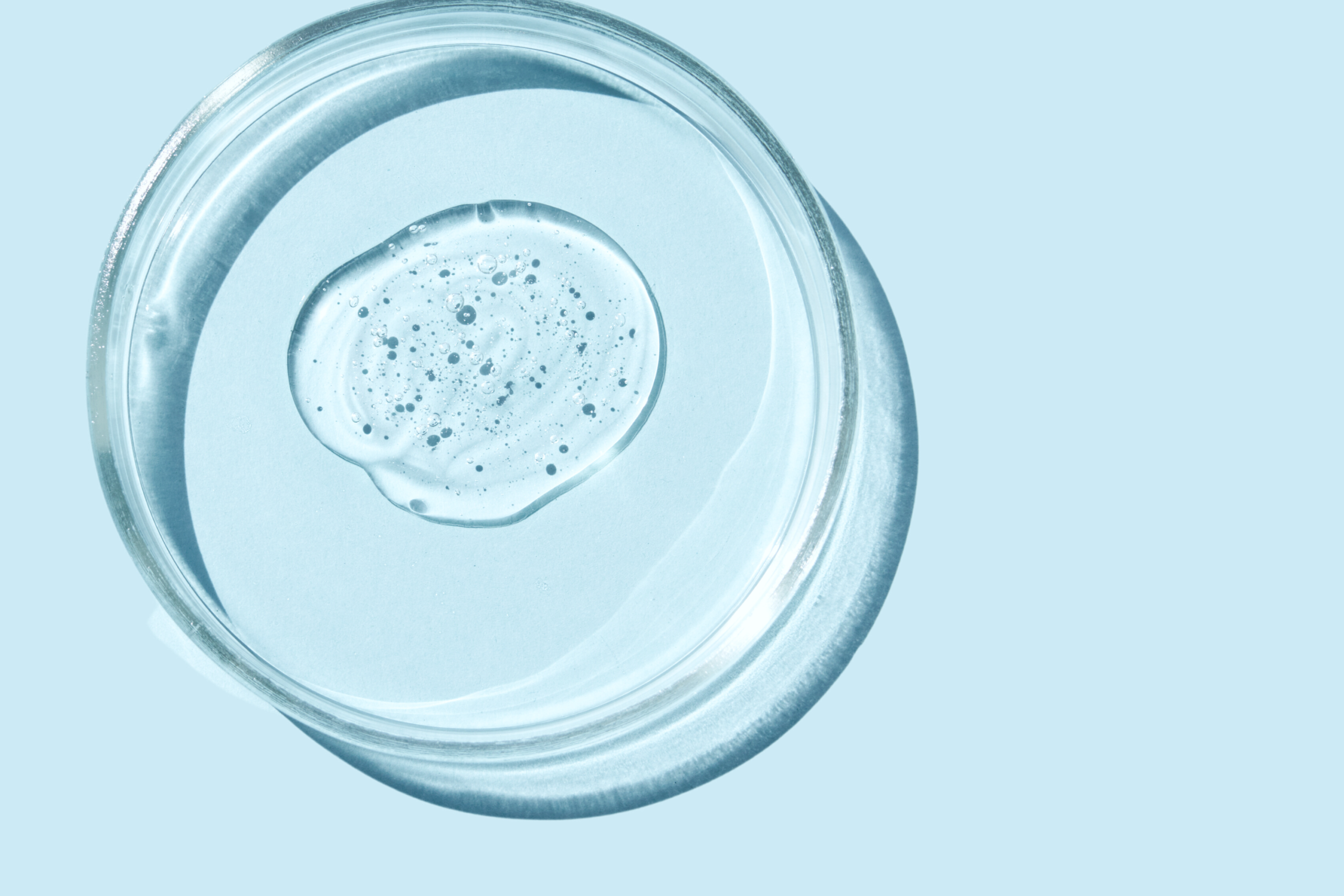 A close up of a drop of Salicylic Acid, a clear substance and natural skin care ingredient, displayed on top of a pale blue background.