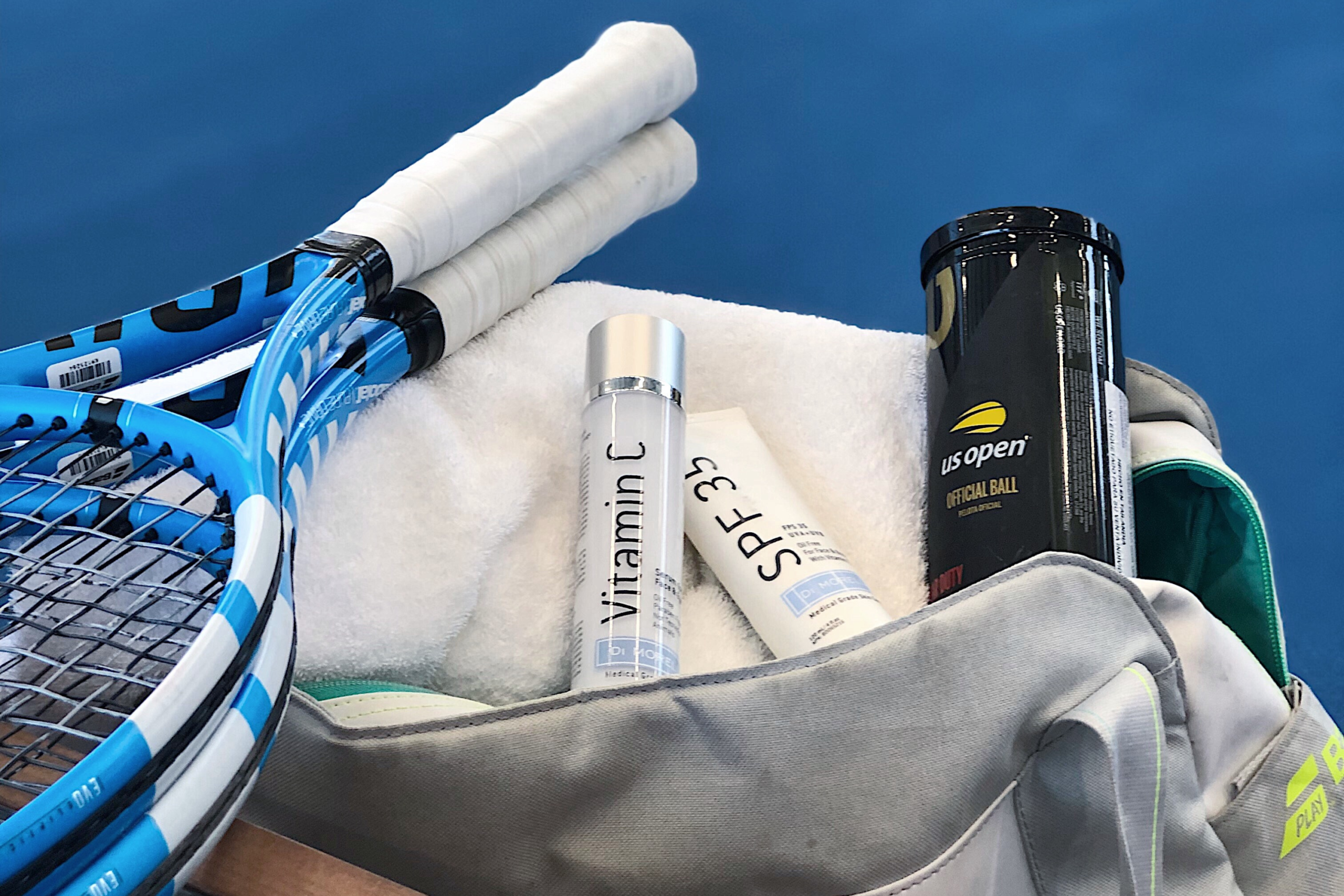 A medium shot of a gym bag featuring skin care products, a tennis racquet and tennis balls.