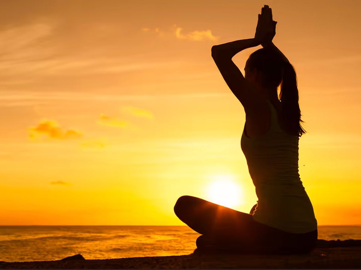 Silhouette of a person performing yoga at sunset by the water.