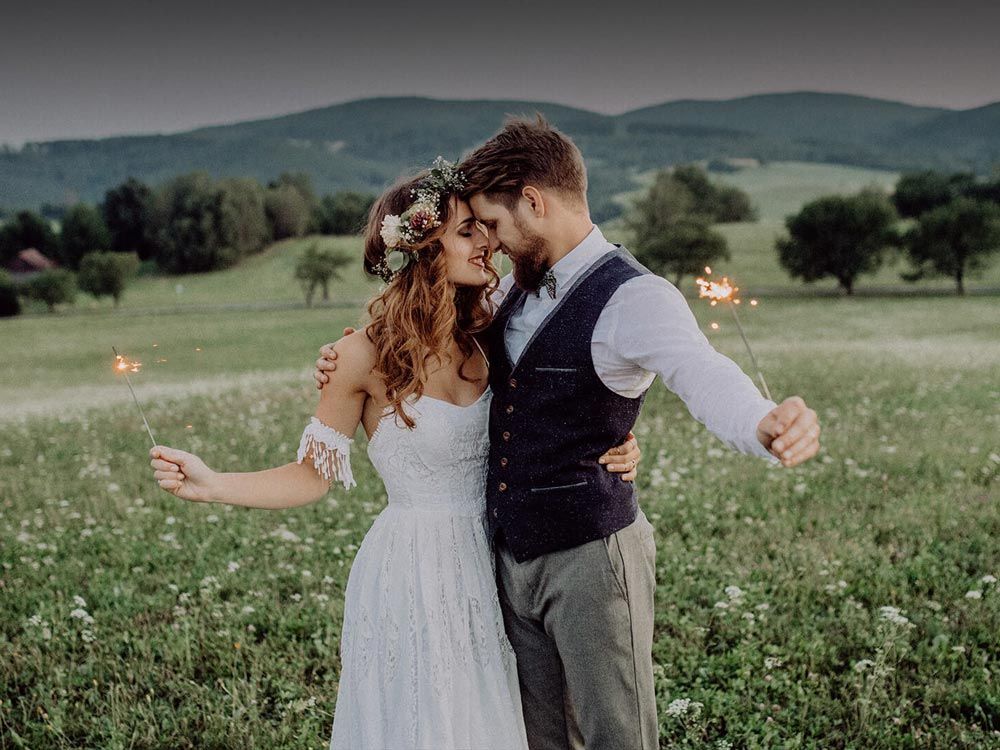 Newlywed couple embraces in a twilight field, holding sparklers, celebrating their wedding.