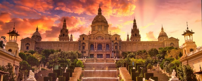 Palau Nacional museum with grand staircase and fountains under dramatic orange sunset sky in Barcelona