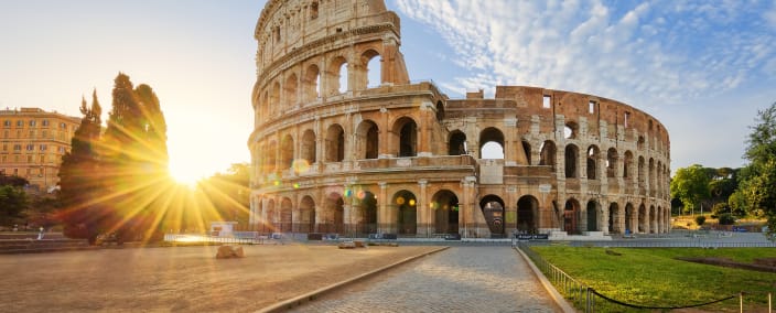 The ancient Roman Colosseum bathed in golden sunset light with dramatic sky and cobblestone foreground