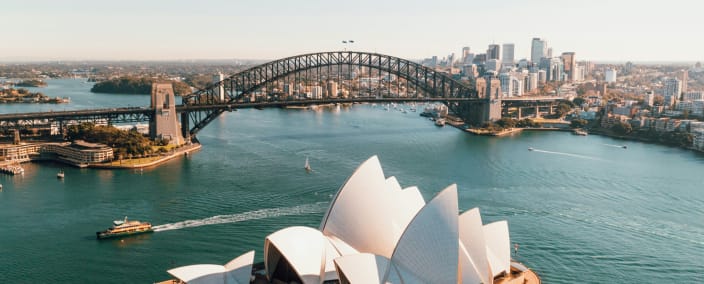 Aerial view of Sydney Opera House and Harbour Bridge with city skyline and turquoise harbor waters