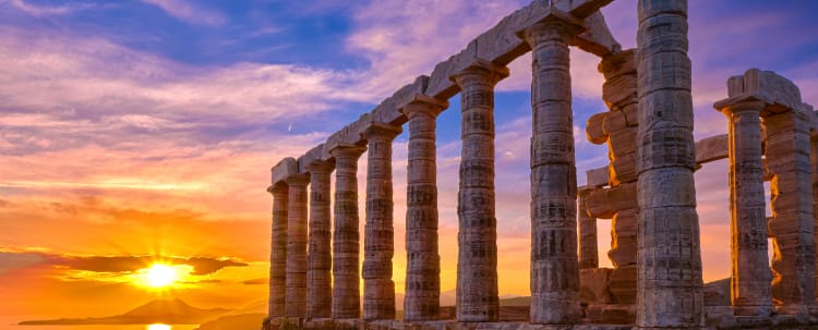 Ancient Greek temple columns silhouetted against dramatic sunset sky with golden light reflecting on water