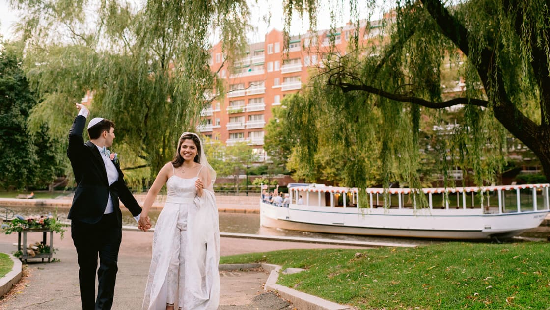 bride and groom on walkway waving at riverboat behind them