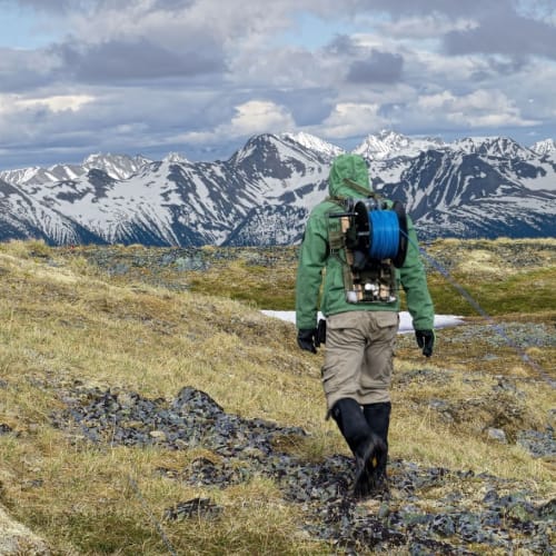 Crew hauling heavy IP cable reels across alpine terrain at Sidina