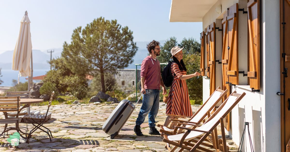 Ζευγάρι φτάνει σε εξοχική κατοικία με βαλίτσες, έτοιμο για διαμονή σε τουριστικό κατάλυμα στην Ελλάδα.