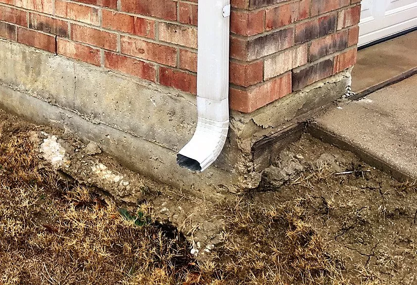 Foundation water damage caused by overflowing gutters showing erosion and structural concerns
