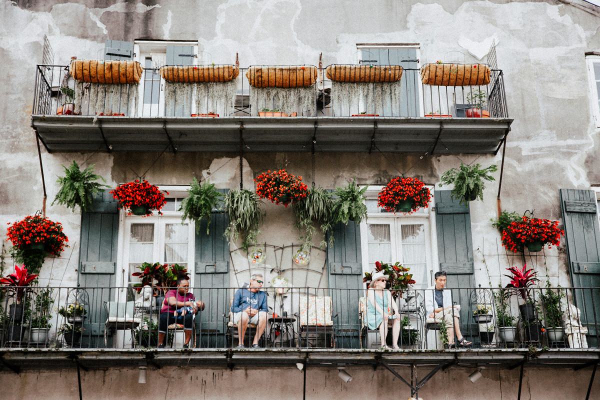 A picturesque New Orleans balcony scene with people relaxing and colorful floral decorations.