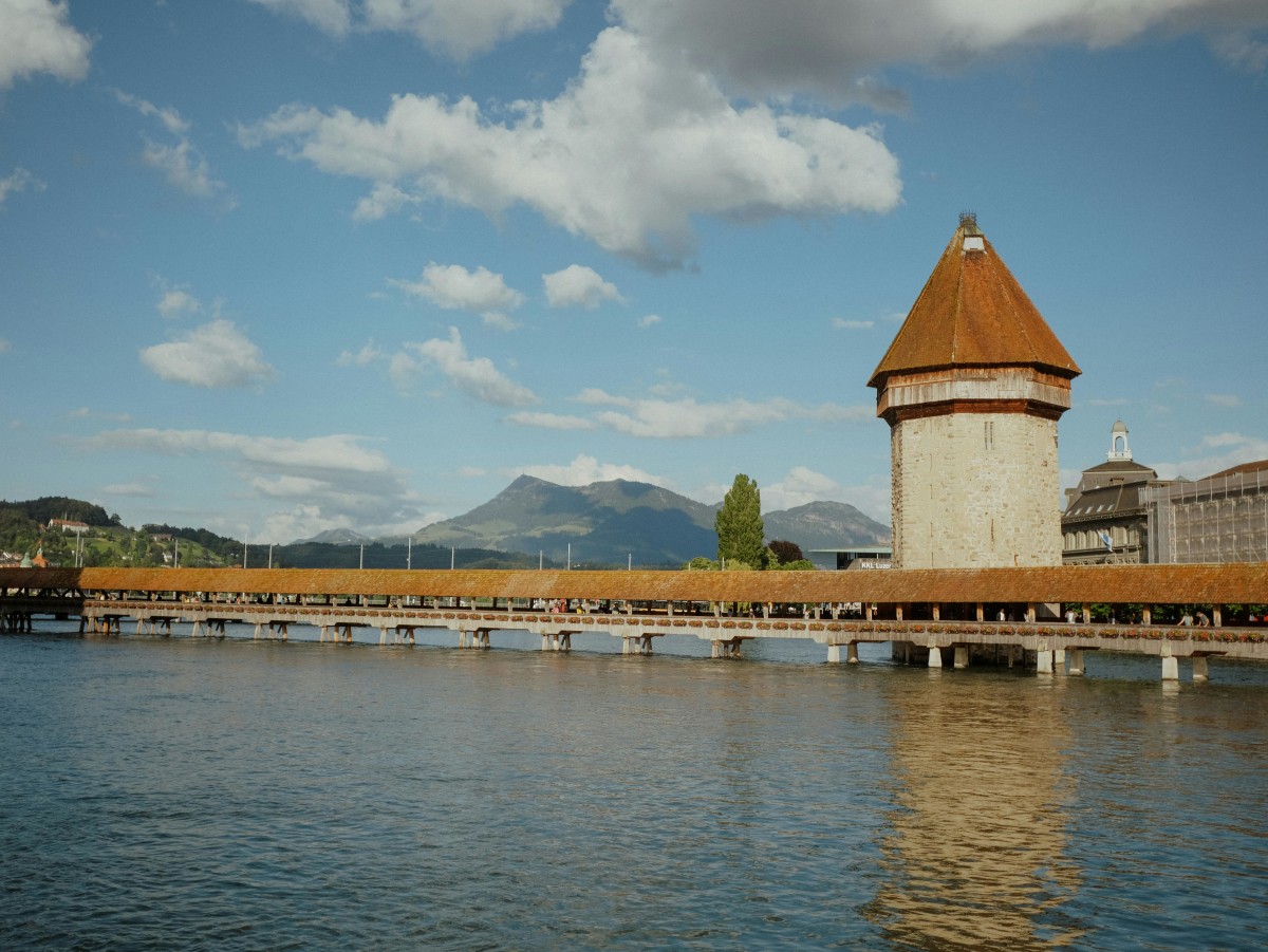 Scenic view of the historic Chapel Bridge and tower in Lucerne, reflecting in the Reuss River on a sunny day.