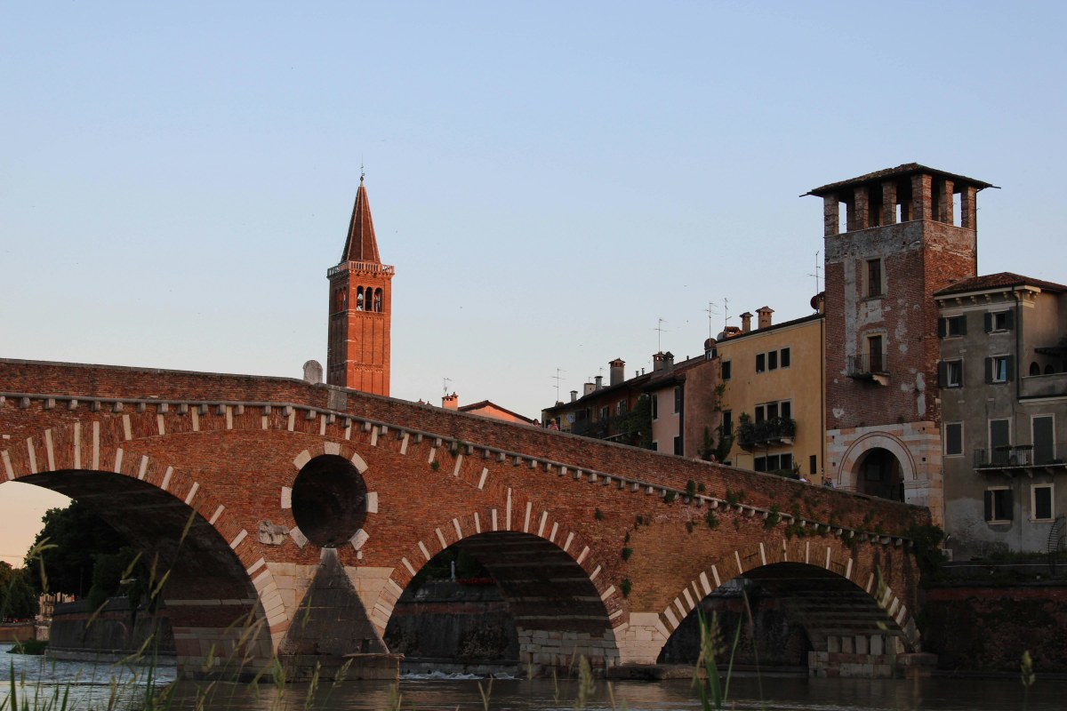 Capture of the iconic Ponte Pietra bridge and bell tower under the warm glow of sunset in Verona, Italy.