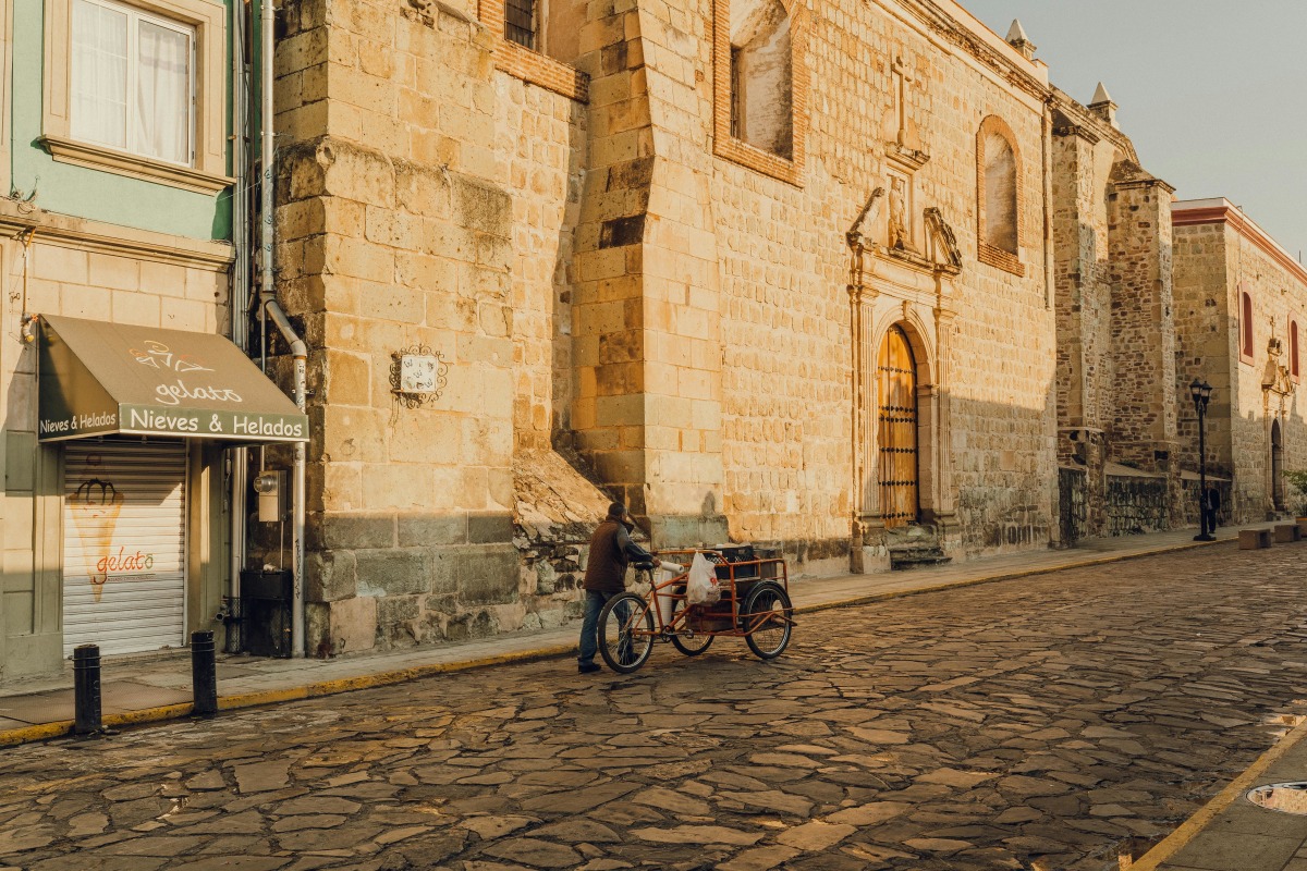 Quiet street in Oaxaca, México featuring historic stone buildings and a local man with a bicycle cart.
