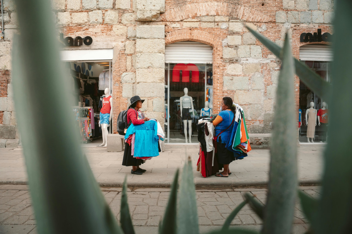 Colorful street scene in Oaxaca featuring local vendors selling clothing near a boutique.