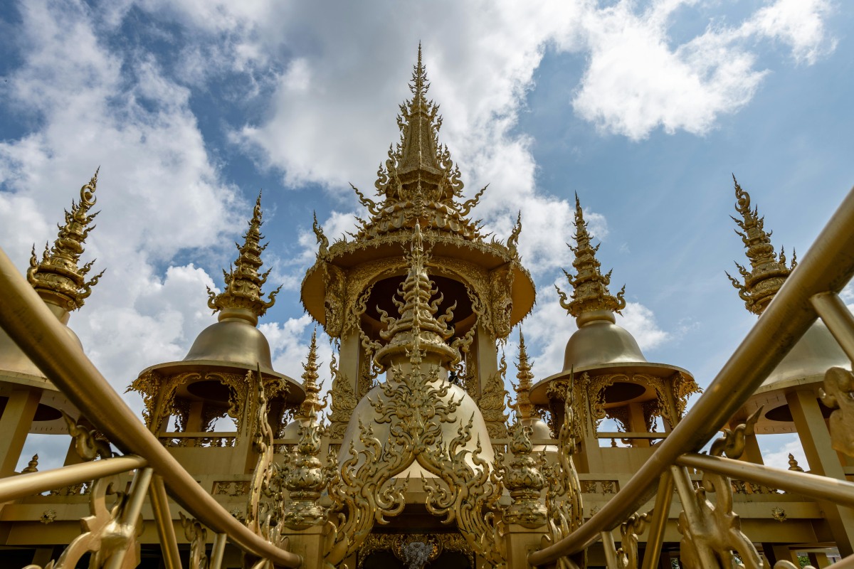 Stunning golden temple architecture in Chiang Rai, Thailand under a bright blue sky.