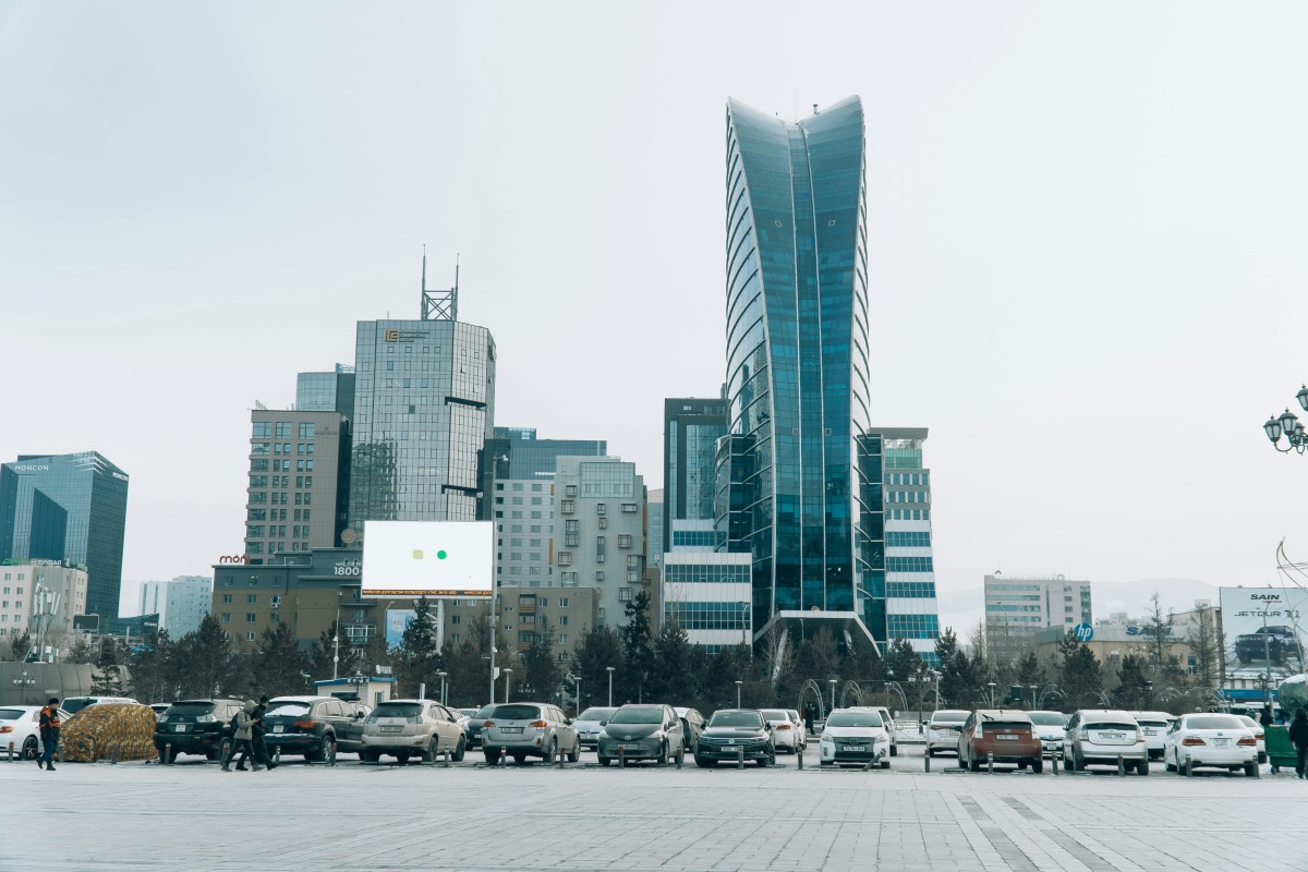View of modern skyscrapers in Ulaanbaatar with parked cars in the foreground, showcasing urban development.