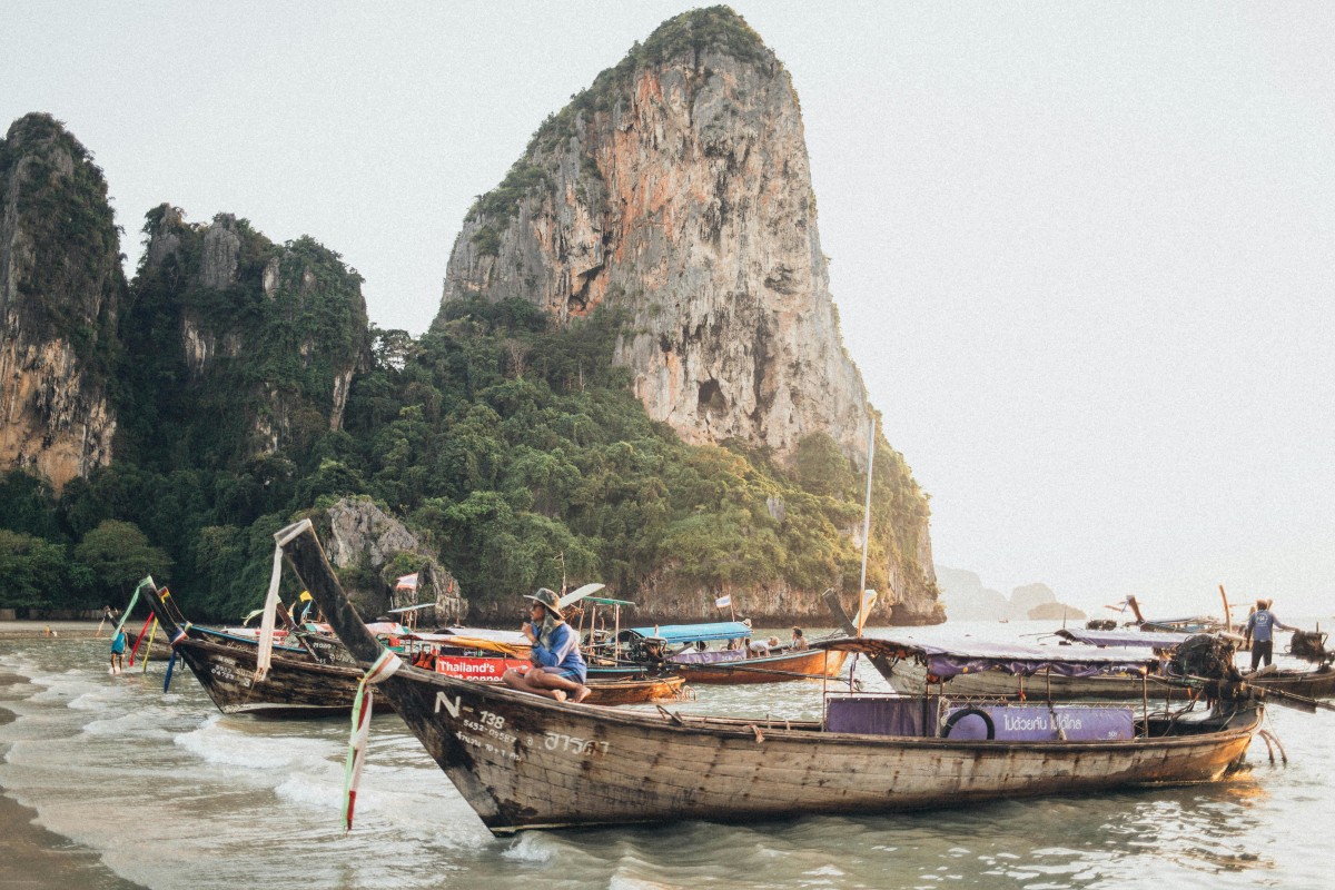 Explore the stunning scenery and traditional long-tail boats in Krabi, Thailand with majestic limestone cliffs in the background.