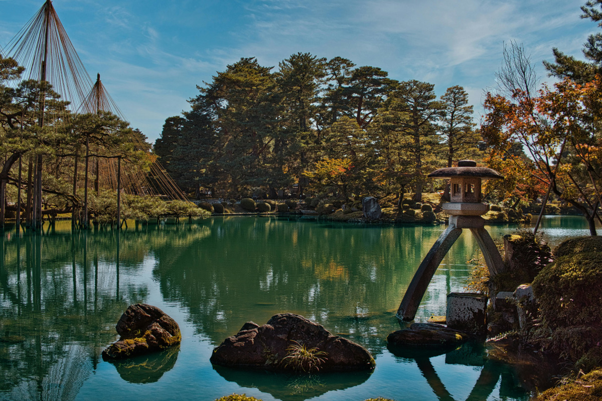 Serene landscape of Kenrokuen Garden with traditional lantern and tranquil pond in Kanazawa, Japan.